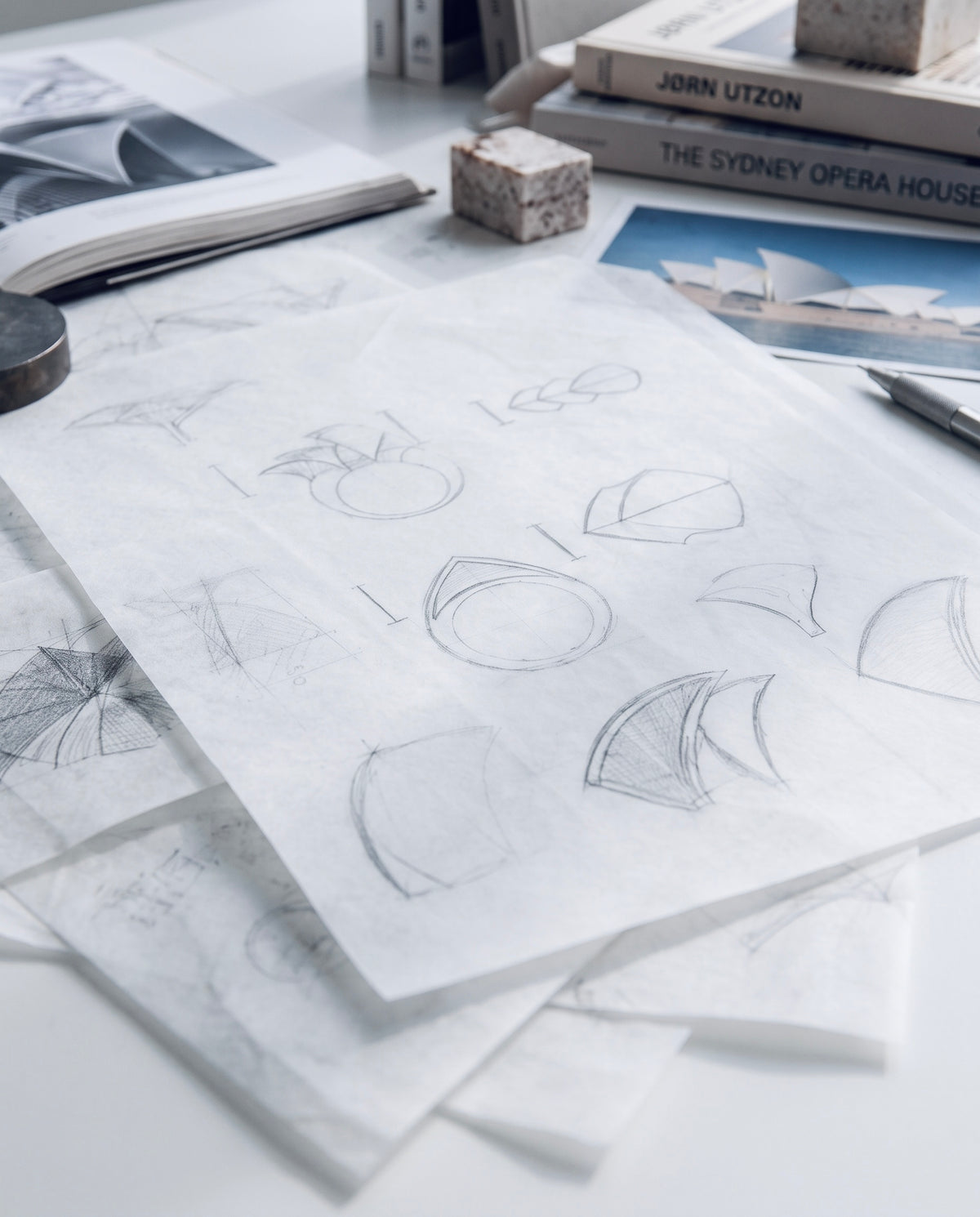 pencil studies for a fenda design on tracing paper, beside architecture books on the studio table